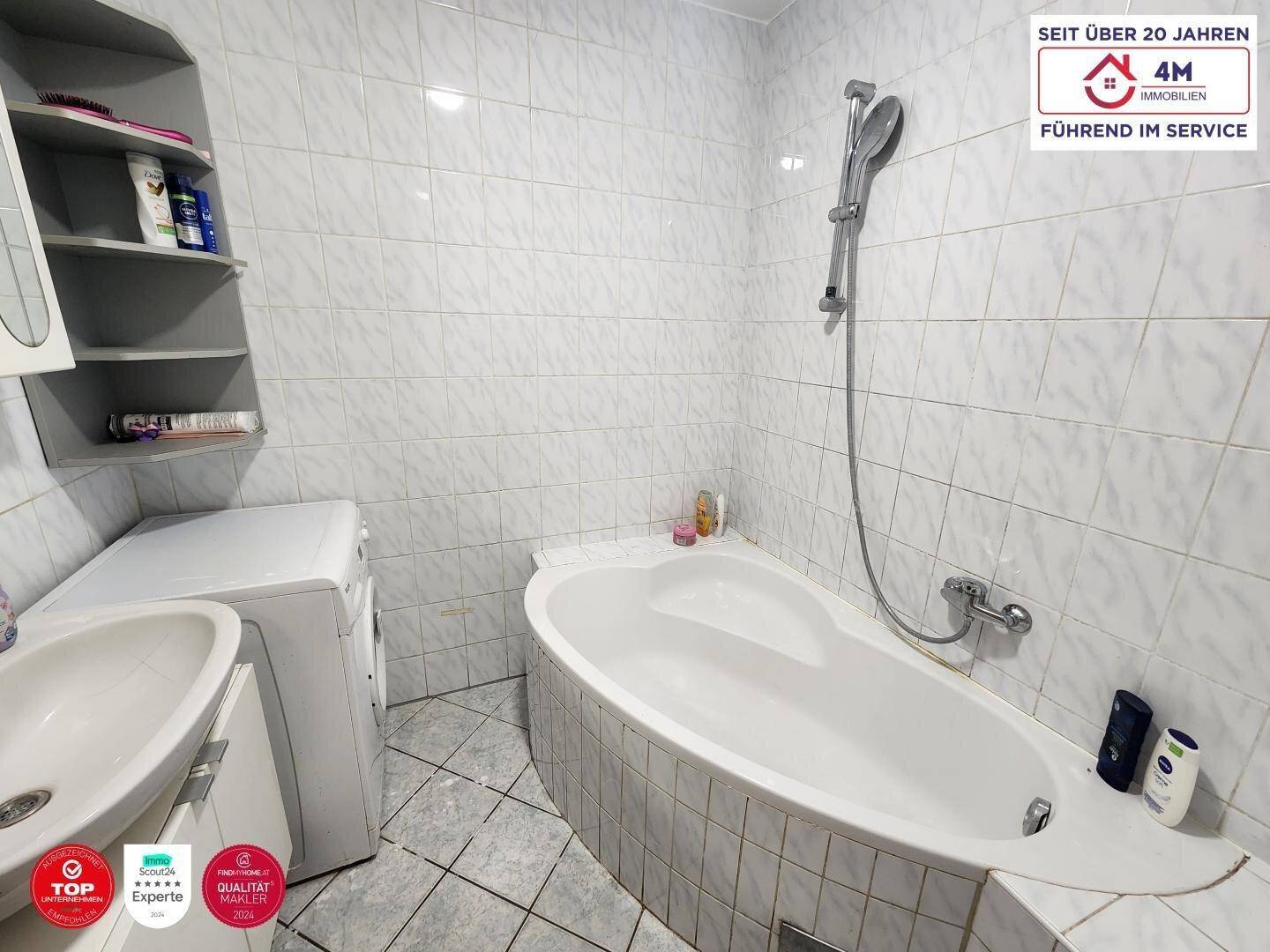 Gefliestes Badezimmer mit Badewanne, Waschbecken und Platz für eine Waschmaschine.