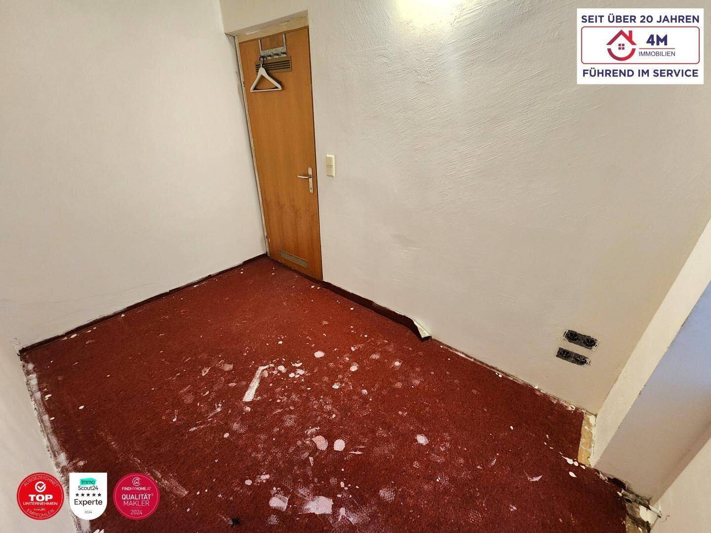 Zimmer mit teilweise entferntem Teppichboden und einer Holztür, bereit für Renovierung.