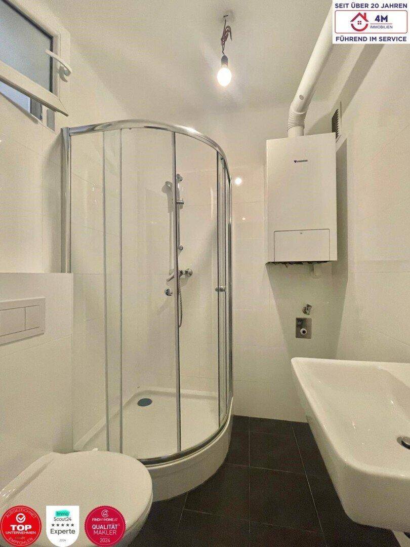 Modernes Badezimmer mit Duschkabine, WC, Waschbecken und wandmontiertem Warmwasserbereiter.