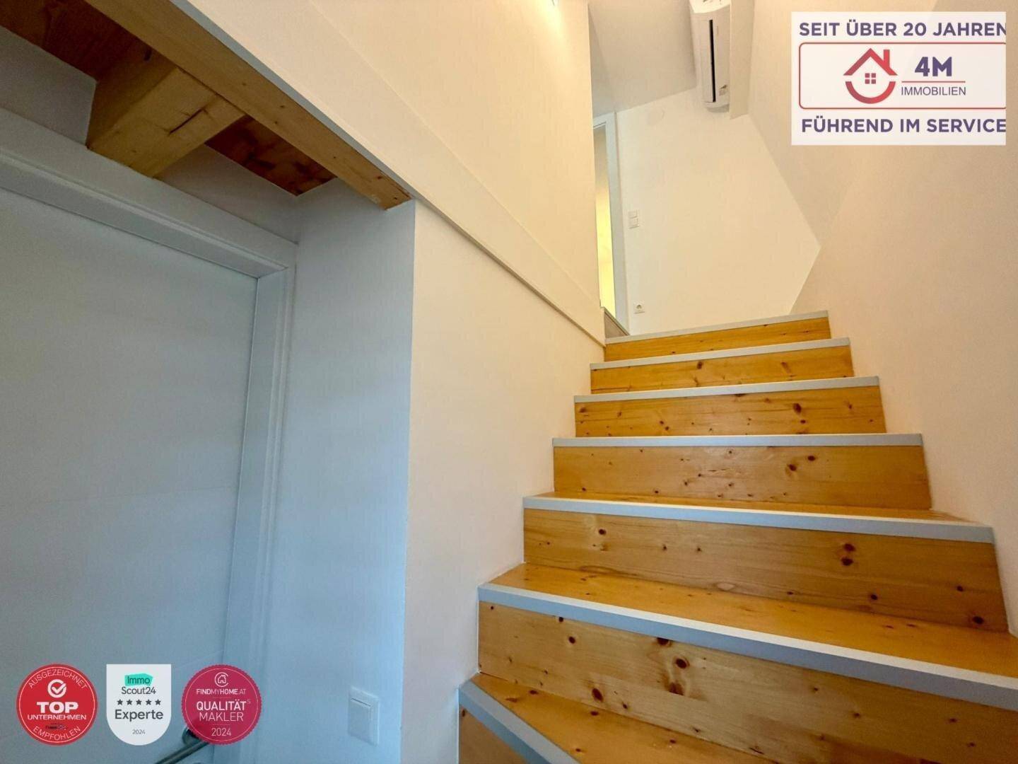 Holztreppe führt in das Obergeschoss, mit hellem Anstrich und Holzbalken.