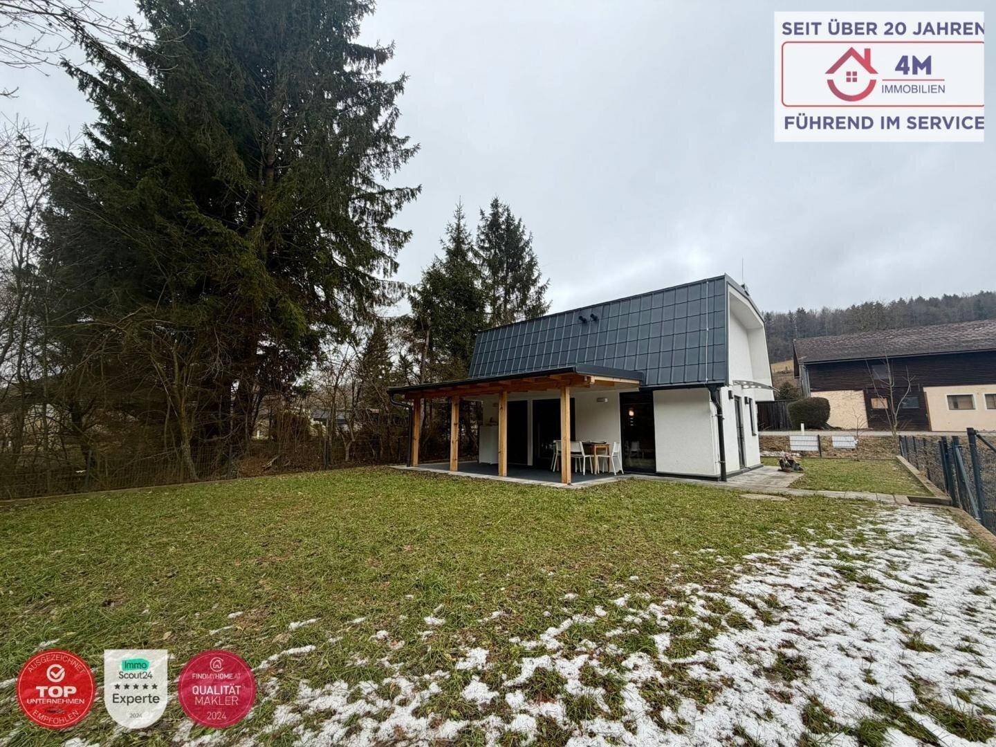 Gartenansicht des Hauses mit überdachter Terrasse und weitläufiger Rasenfläche.