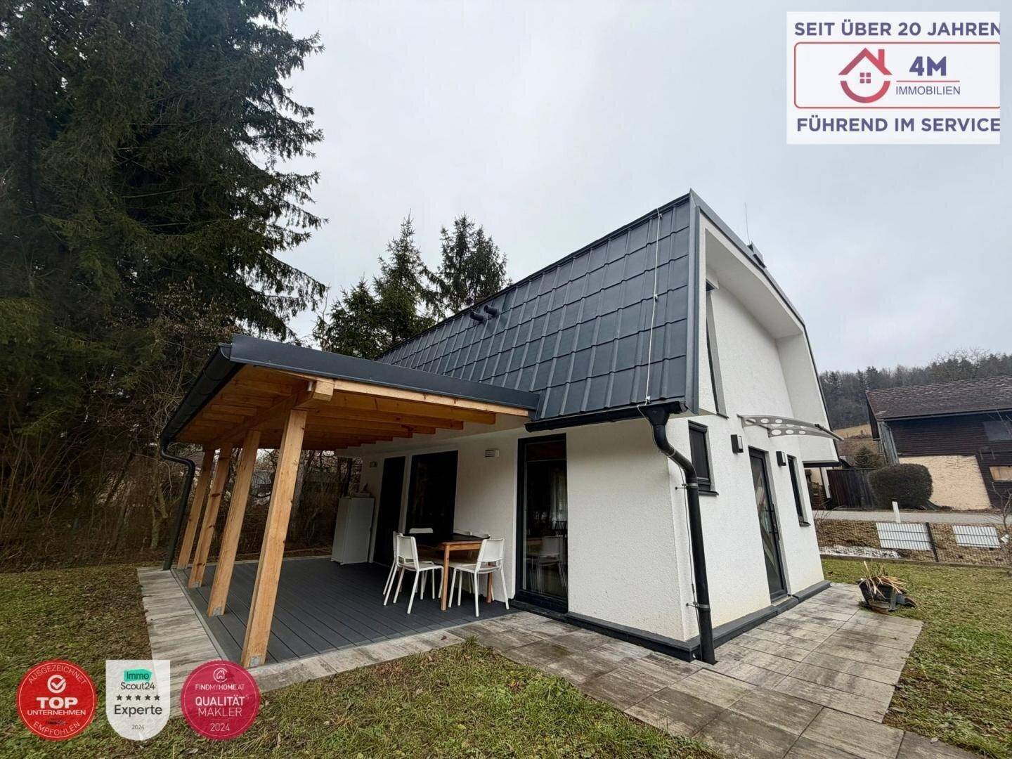 Überdachte Terrasse mit Holzbalken und Sitzgelegenheiten neben dem modernen Haus.