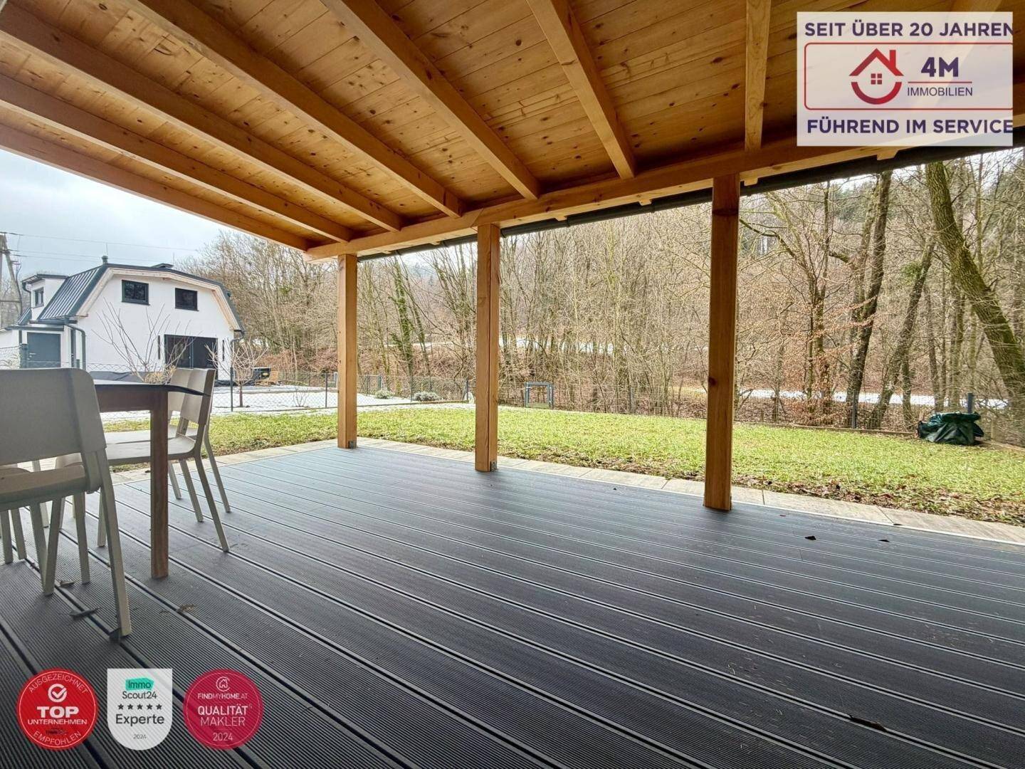 Geräumige überdachte Terrasse mit Holzbalken und Blick auf den Garten und das Haus.