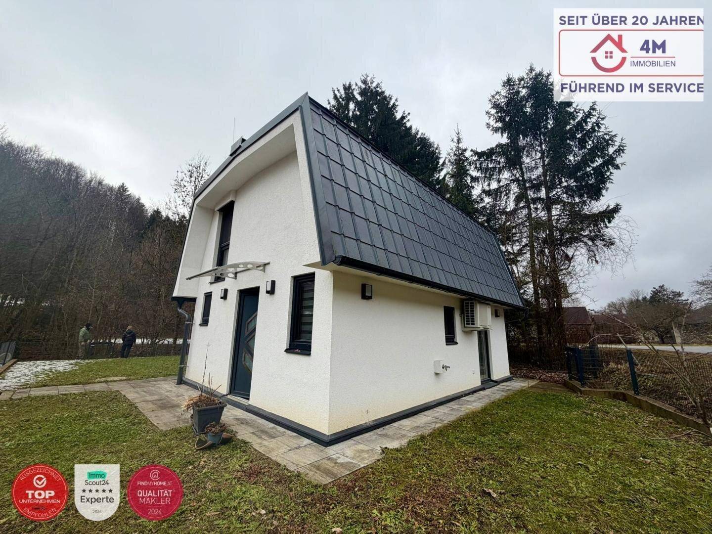 Seitenansicht des modernen Hauses mit dunklem Dach und Klimaanlage an der Fassade.