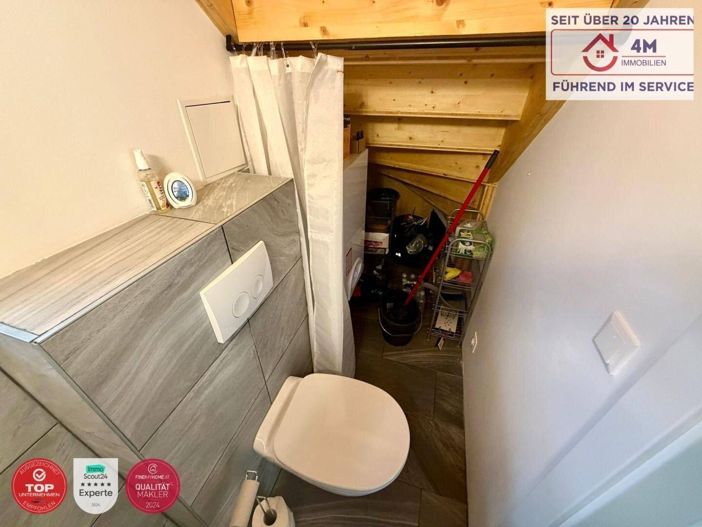 Gäste-WC mit modernen Fliesen, wandhängendem WC und Stauraum unter der Treppe.