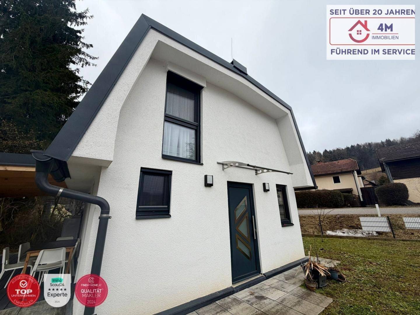 Nahaufnahme der modernen Hausfassade mit Eingangstür und dunklen Fensterrahmen.
