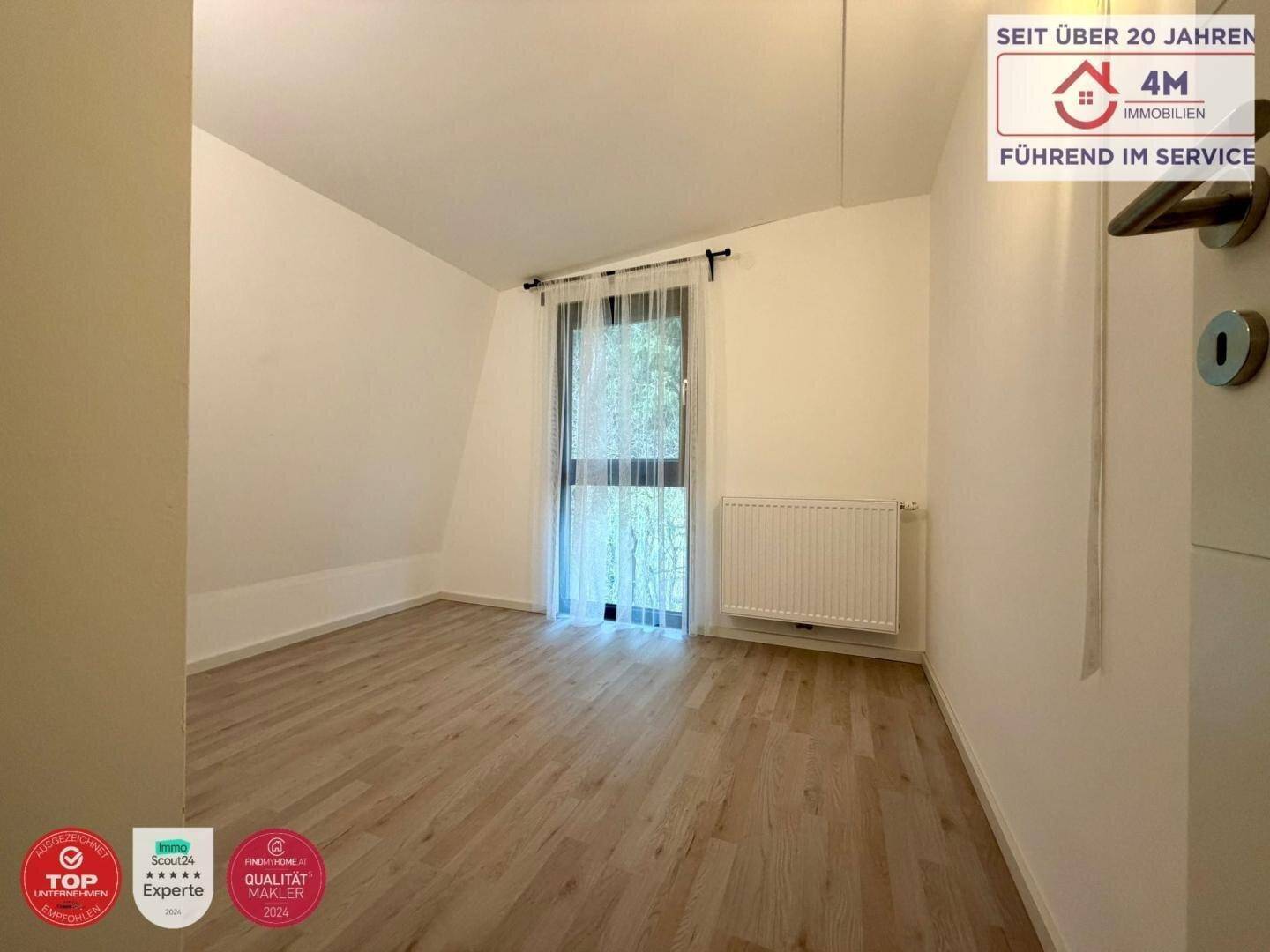 Helles Schlafzimmer im Obergeschoss mit Holzboden und Fenster mit Blick ins Grüne.