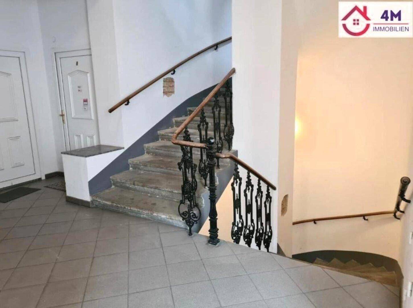Historisches Treppenhaus mit schmiedeeisernem Geländer, Holzhandlauf und Steinstufen in einem Altbau.
