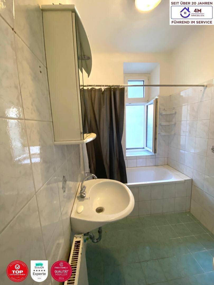 Badezimmer mit Badewanne, Waschbecken, Spiegelschrank und Fenster, im Stil der 80er Jahre.