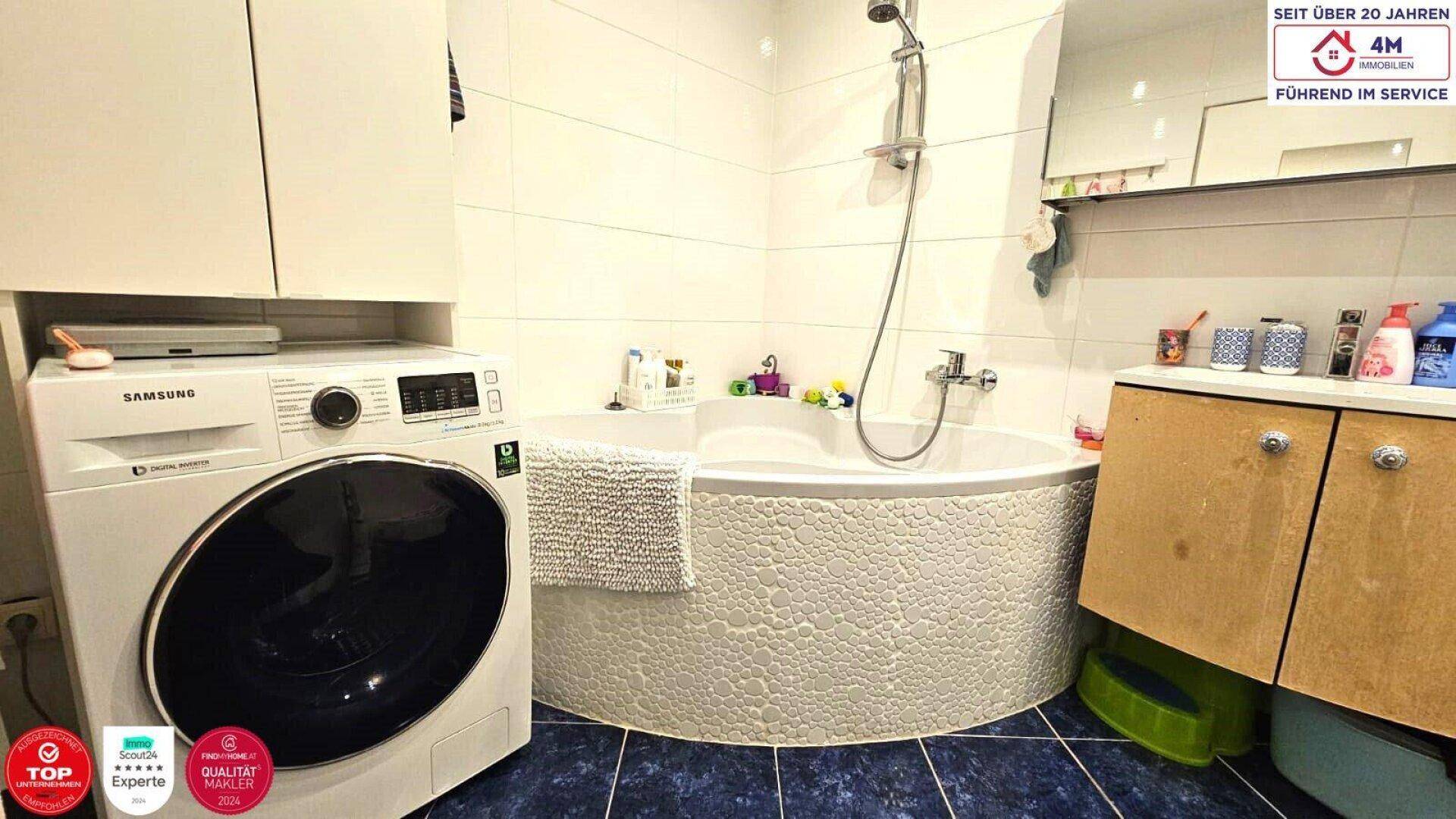 Badezimmer mit Eckbadewanne, Waschmaschine und blauen Fliesen, praktisch und hell gestaltet.