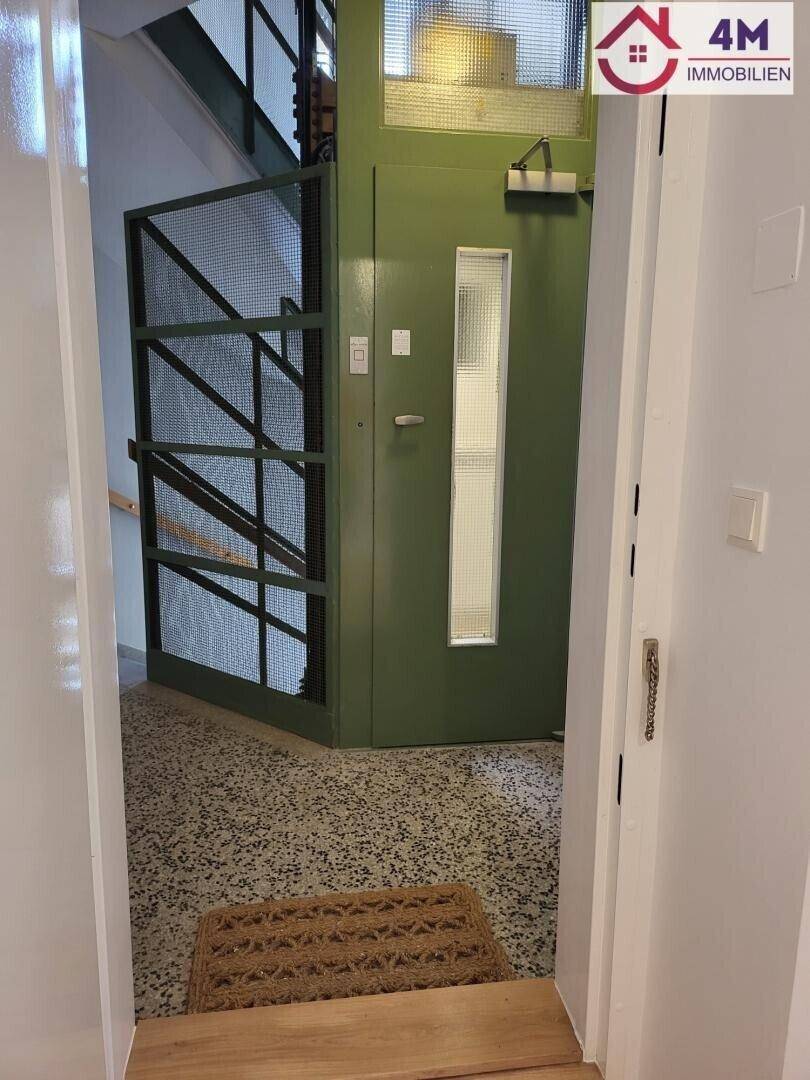 Alter, funktionaler Aufzug in einem Treppenhaus mit Terrazzoboden und Gittertür.