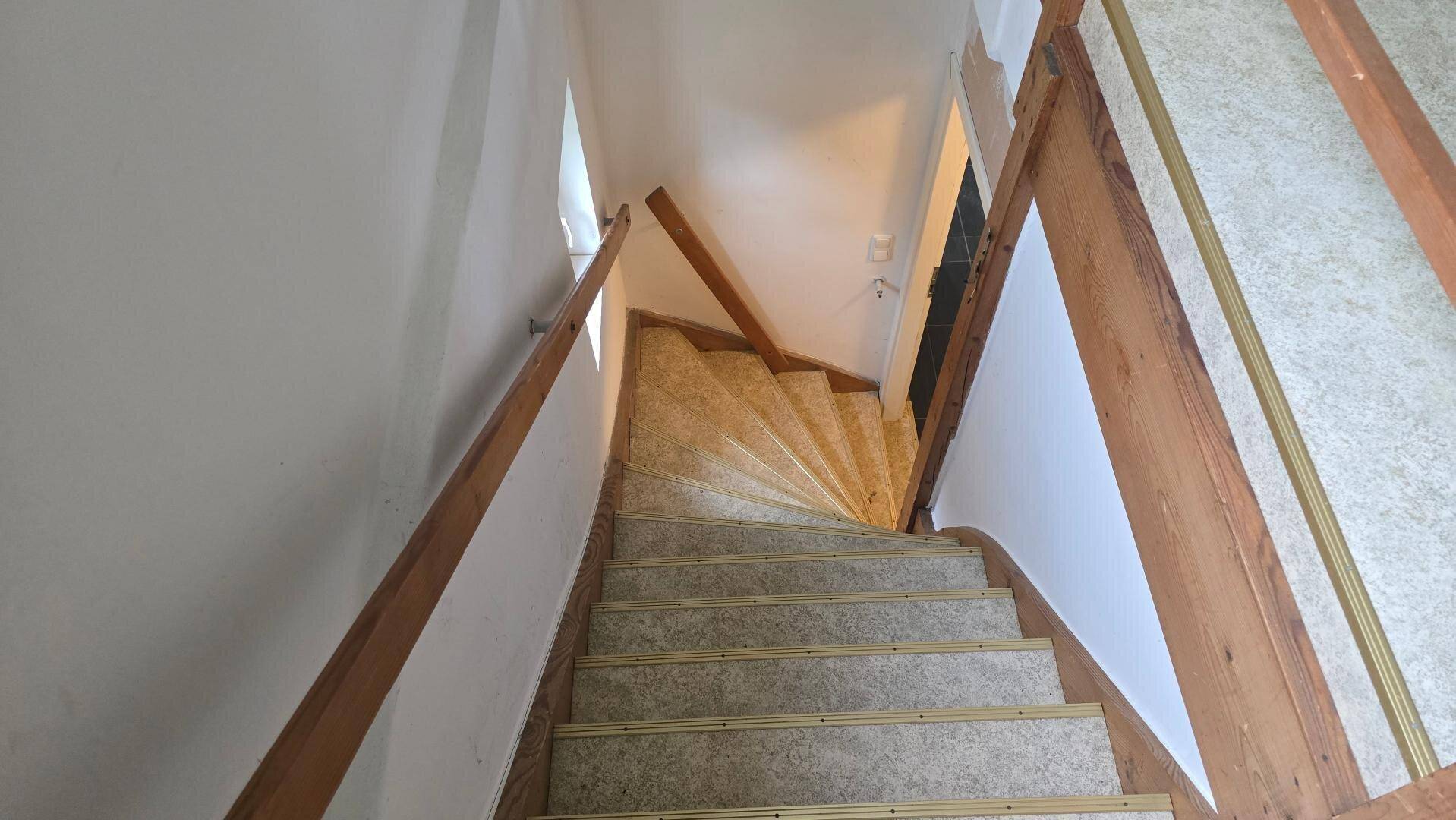 Treppenhaus mit Holzgeländer und Teppichstufen, führt in die oberen Etagen.
