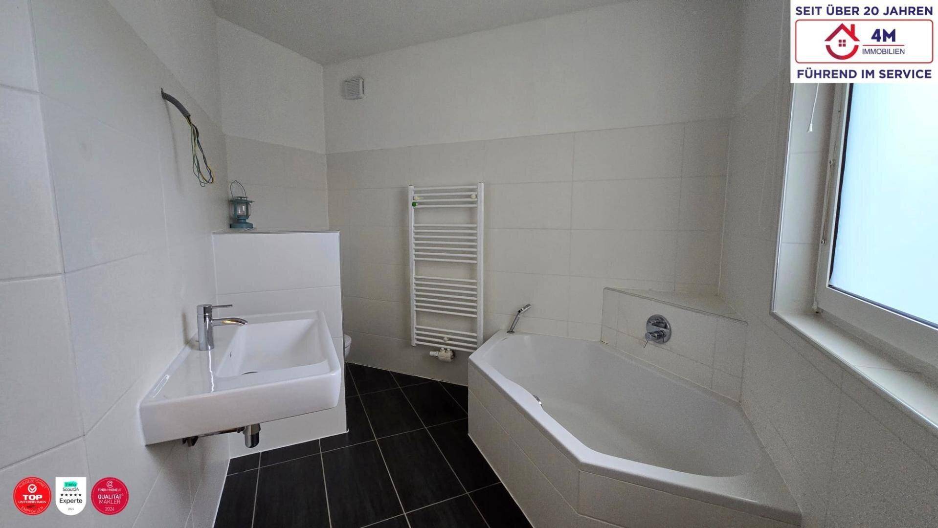 Modern gefliestes Badezimmer mit Eckbadewanne, wandhängendem Waschbecken und Fenster.
