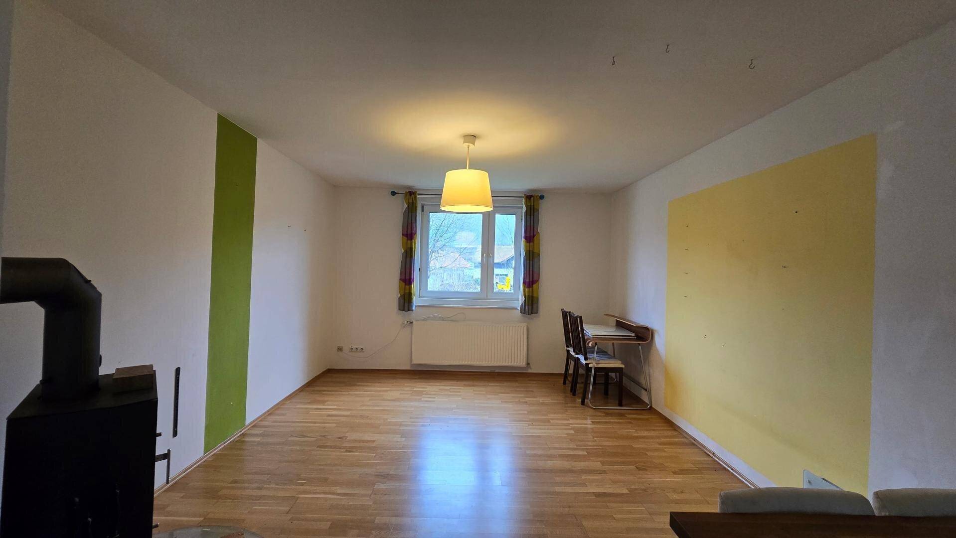 Heller Wohnbereich mit Holzboden, farbigen Akzentwänden und einem Fenster.