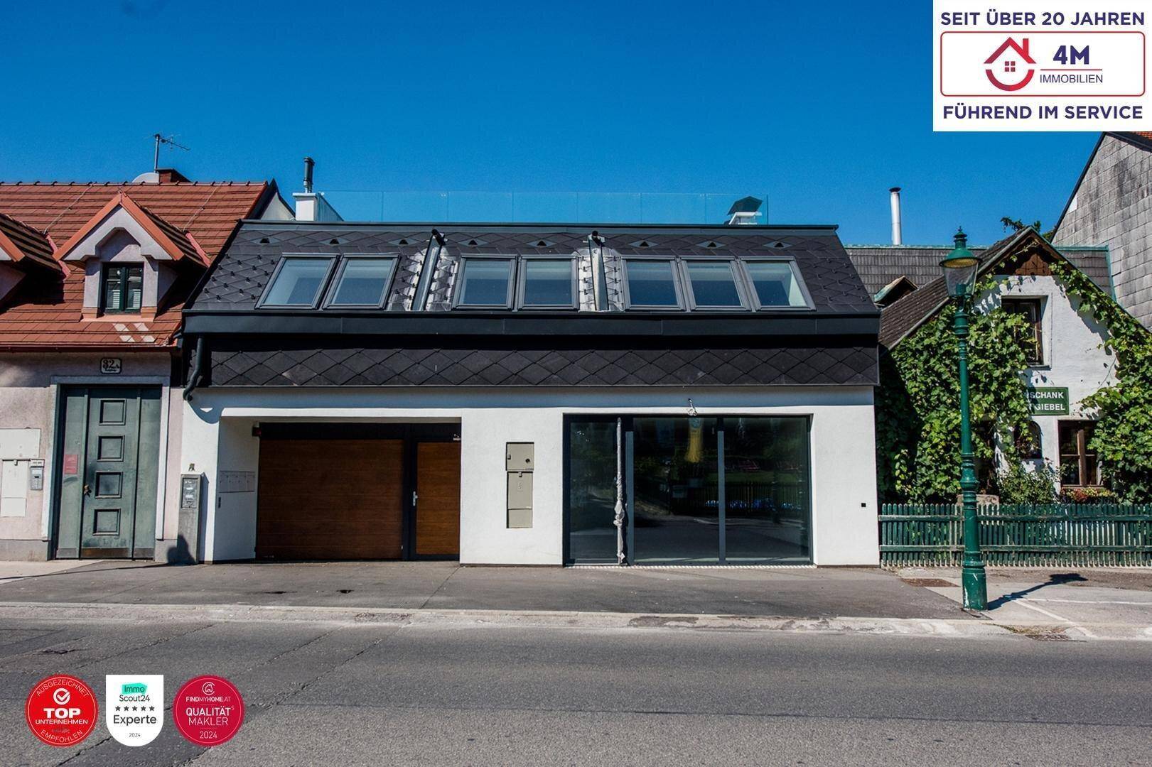 Moderne Gebäudefassade mit großen Fenstern, Garagentor und mehreren Dachfenstern, direkt an der Straße gelegen.