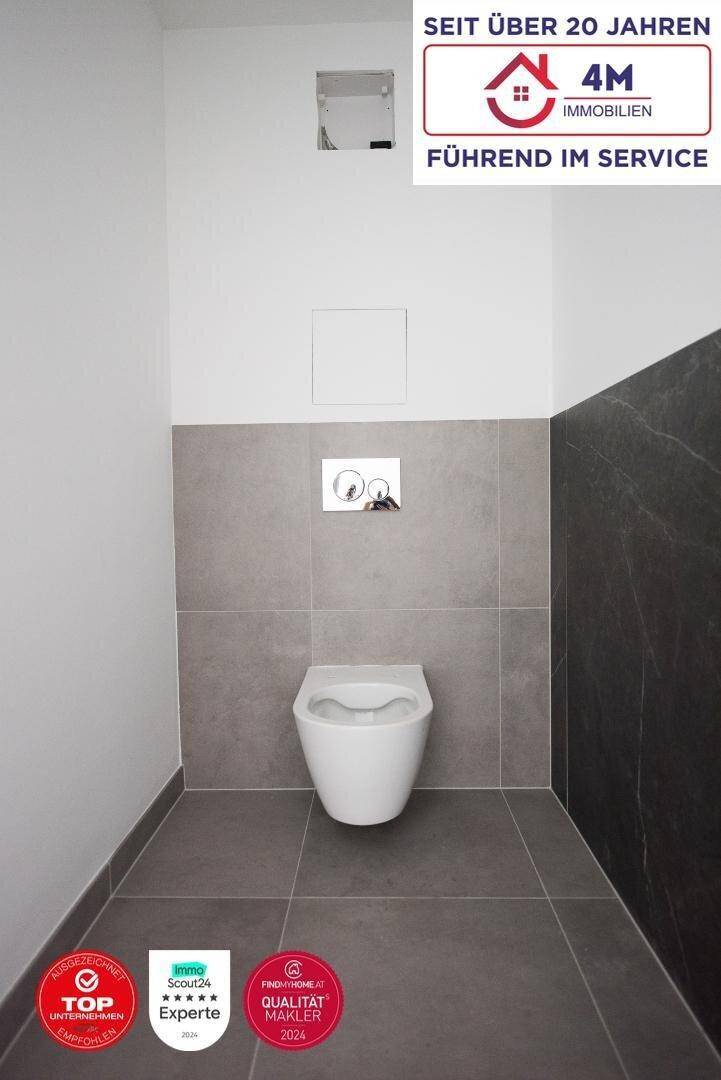 Modernes Gäste-WC mit wandhängender Toilette und stilvollen grauen Fliesen an Boden und Wänden.