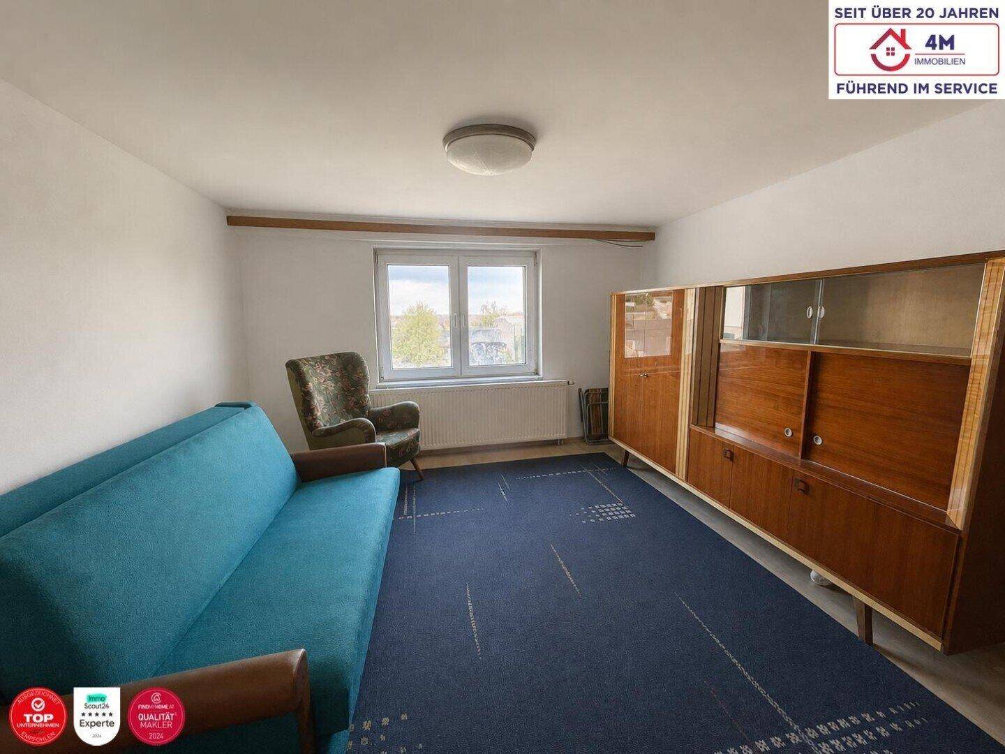Schlafzimmer oder Wohnzimmer mit blauem Teppich, Sofa und einem großen Holzschrank.