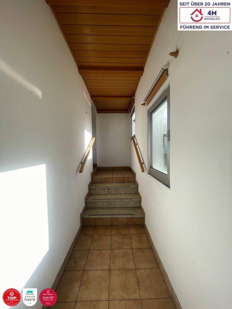 Heller Flur mit Holzdecke, gefliestem Boden und Treppe zum oberen Stockwerk.