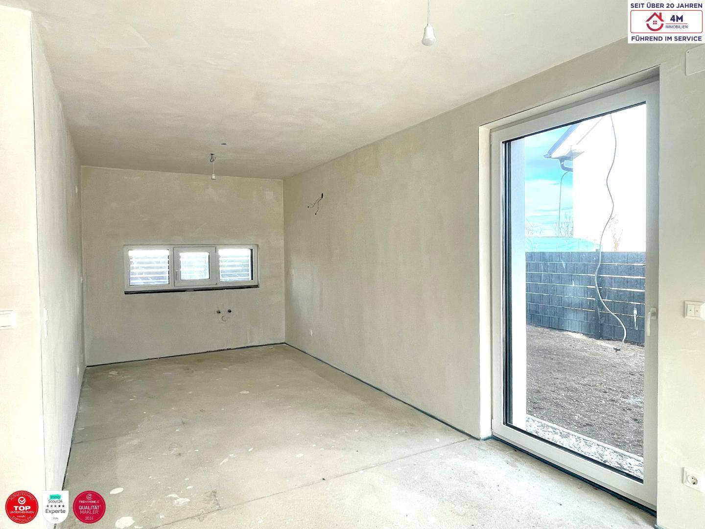 Heller, unfertiger Wohnbereich mit großem Fenster und Blick auf den zukünftigen Garten.