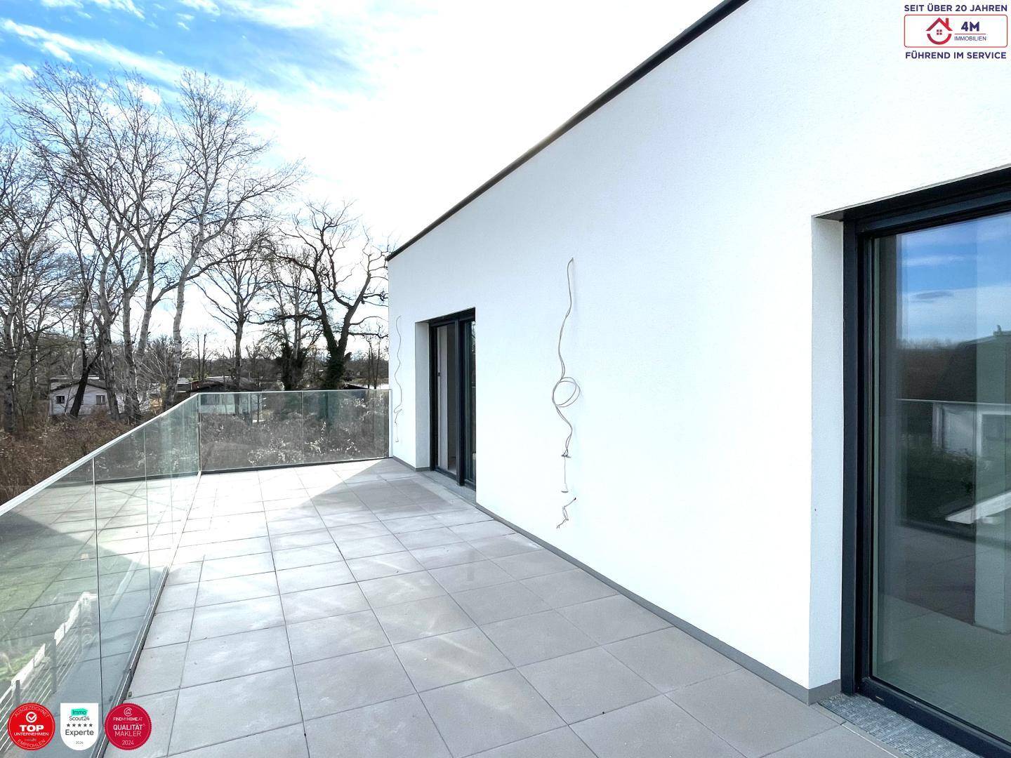 Dachterrasse mit moderner Glasbrüstung und weitem Blick ins Grüne, ideal für Entspannung.