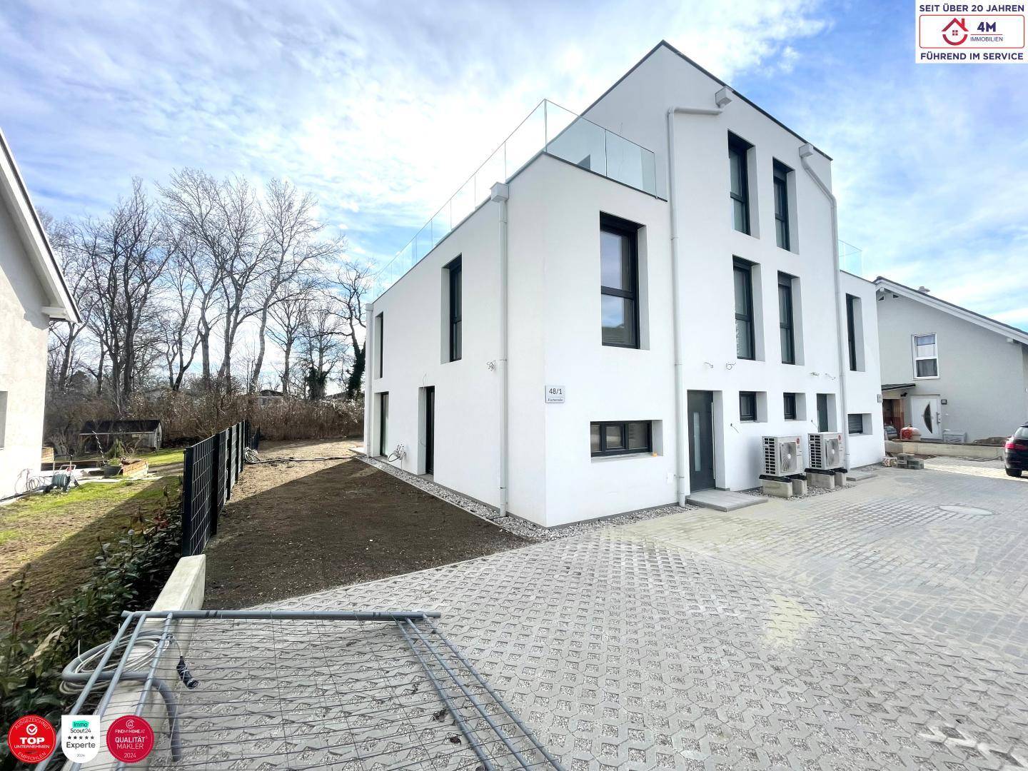 Ansicht der modernen Doppelhaushälfte von der Einfahrtseite mit gepflastertem Bereich und Luftwärmepumpen.