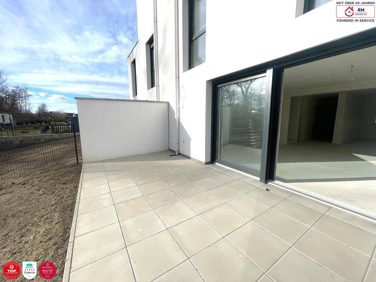 Geräumige, geflieste Terrasse direkt am Neubau, bereit für die Gestaltung eines Außenbereichs.