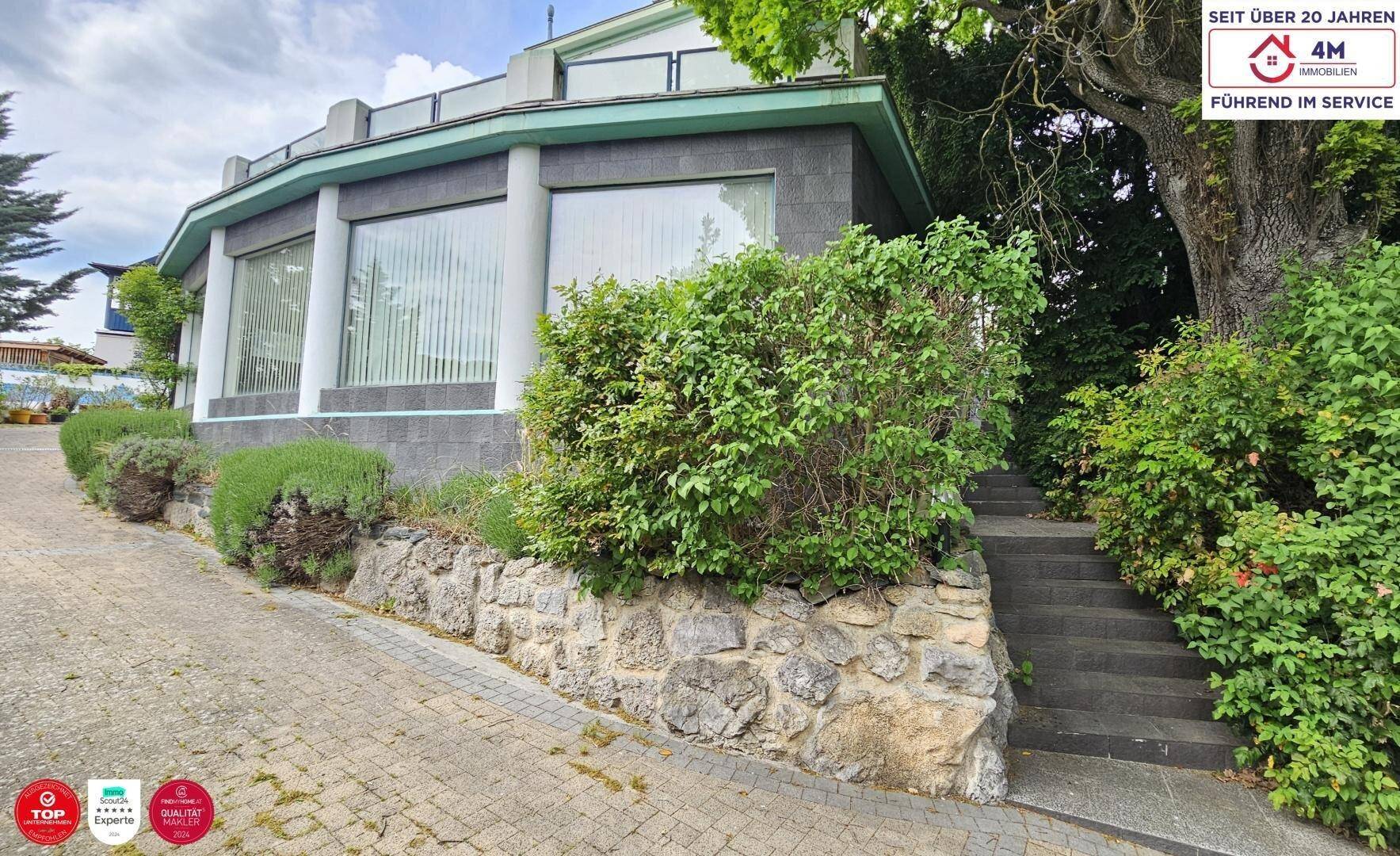 Außenansicht des Gebäudes mit geschwungener Fassade, großen Fenstern und einer Steintreppe im Grünen.