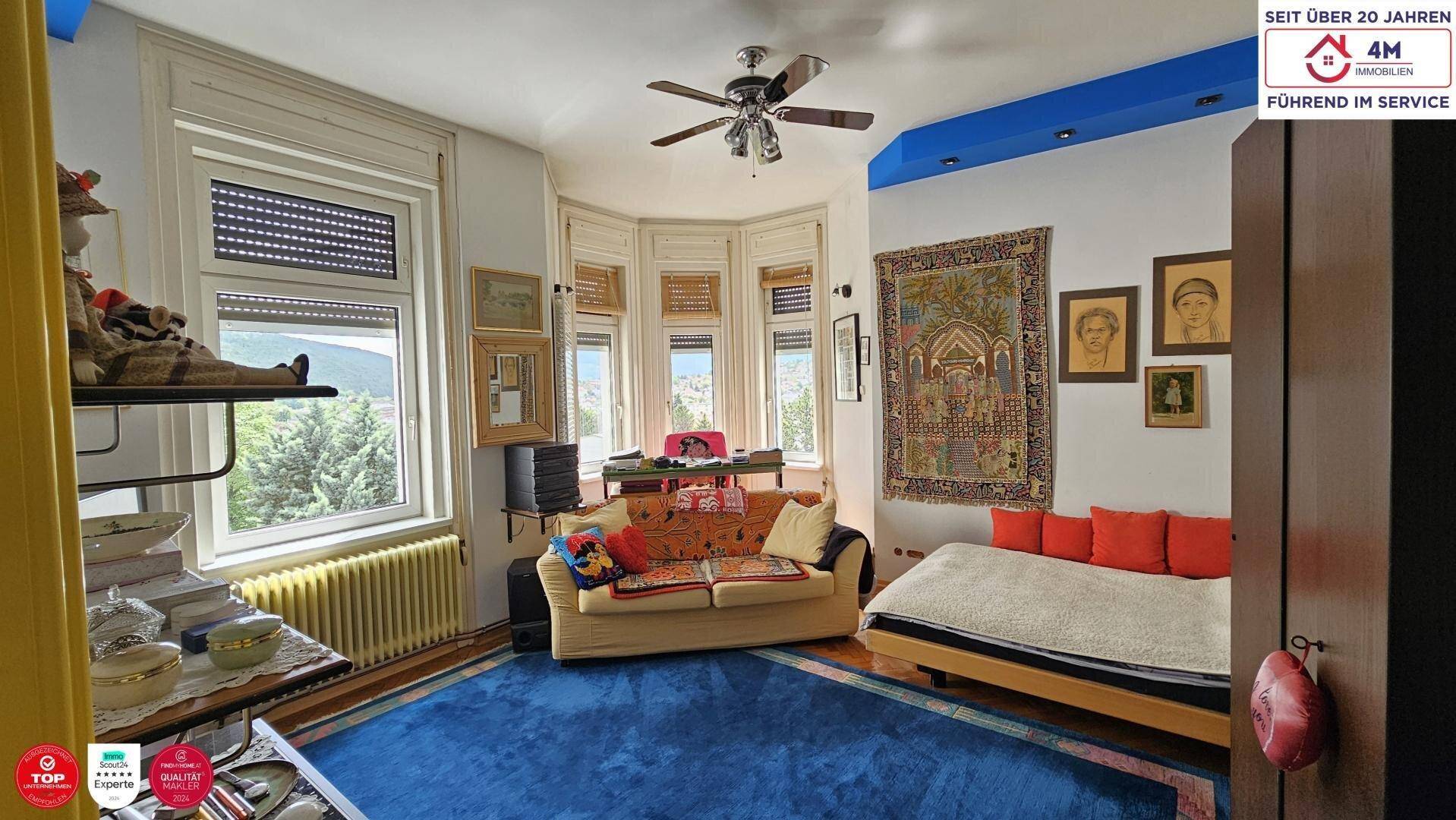 Gemütliches Wohnzimmer mit Erkerfenstern, blauem Teppich und traditioneller Einrichtung.