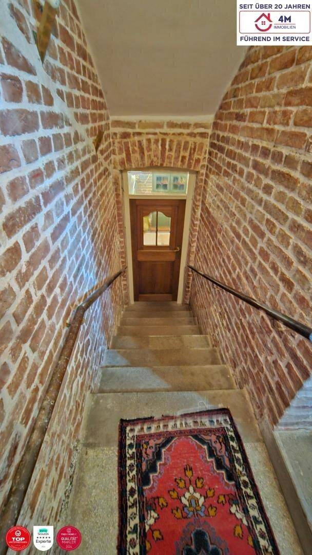 Treppenhaus mit freiliegenden Ziegelwänden, Holzgeländer und einem Teppich, der zu einer Holztür führt.
