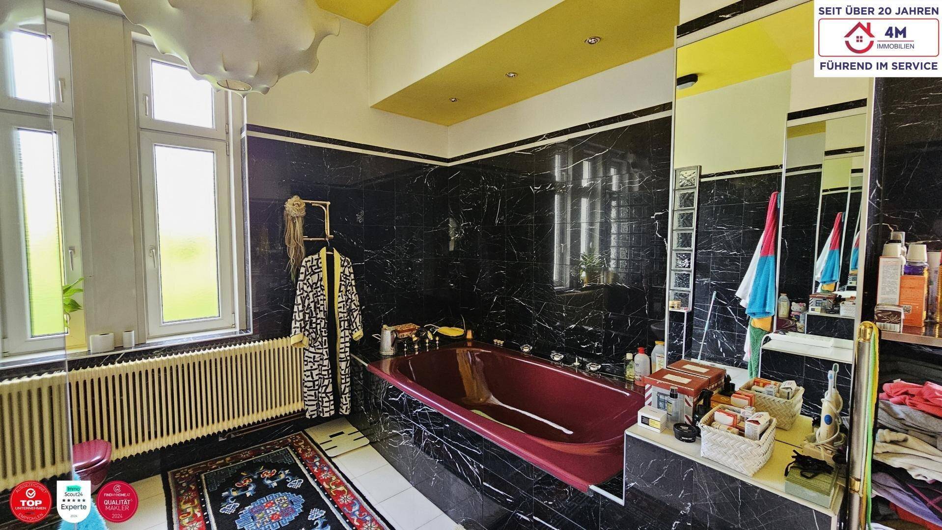 Badezimmer mit schwarzen Marmorfliesen, einer roten Badewanne und einem großen Spiegel.