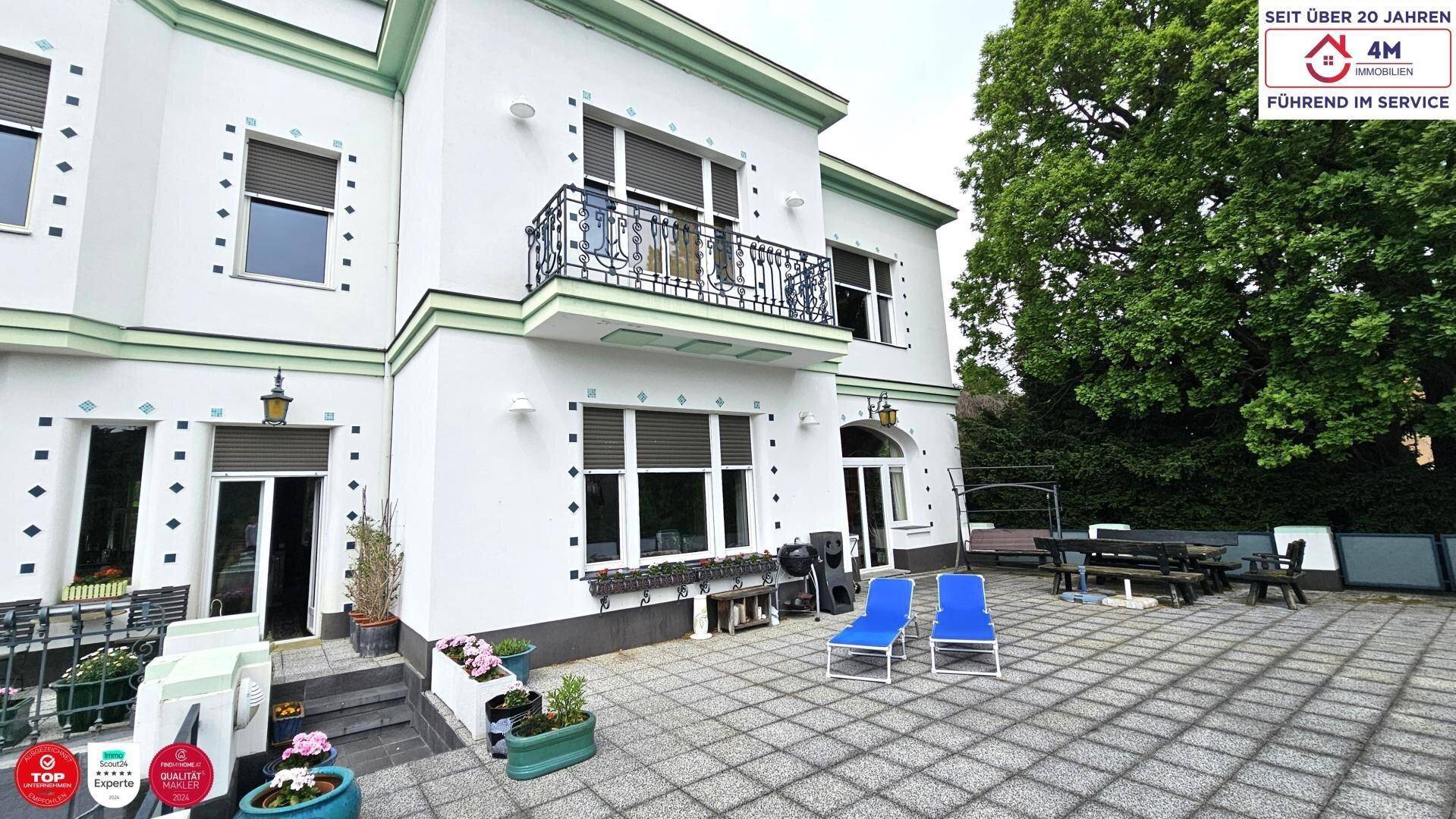 Fassade der Villa mit Balkonen, Fensterläden und einer gepflasterten Terrasse mit Liegestühlen.