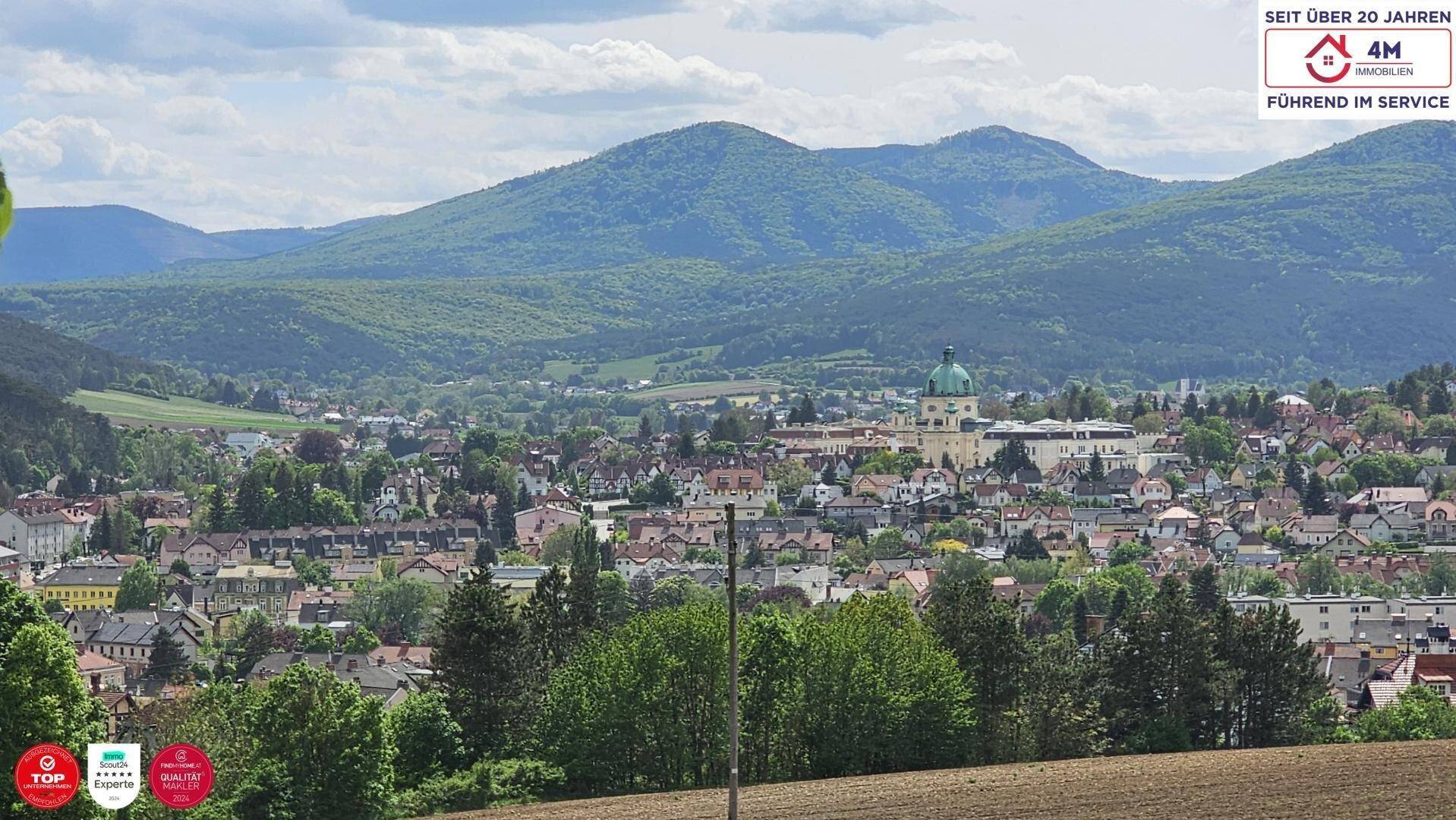 Weitläufiger Blick über eine malerische Stadt im Tal mit grünen Hügeln im Hintergrund.