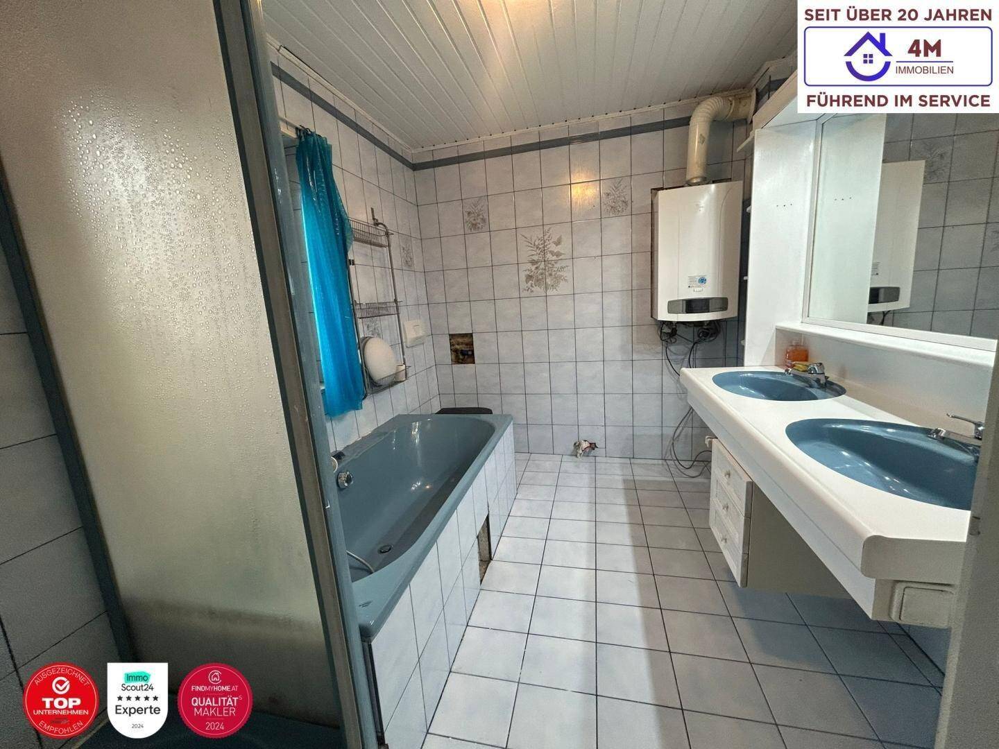 Badezimmer im 80er-Jahre-Stil mit blauen Fliesen, Badewanne und Doppelwaschbecken.