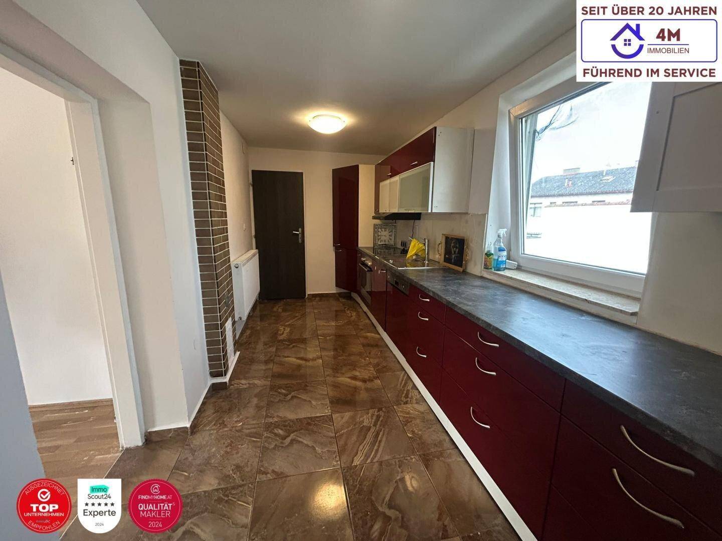 Funktionale Küche mit roten Unterschränken, Fliesenboden und Fenster mit Blick nach draußen.