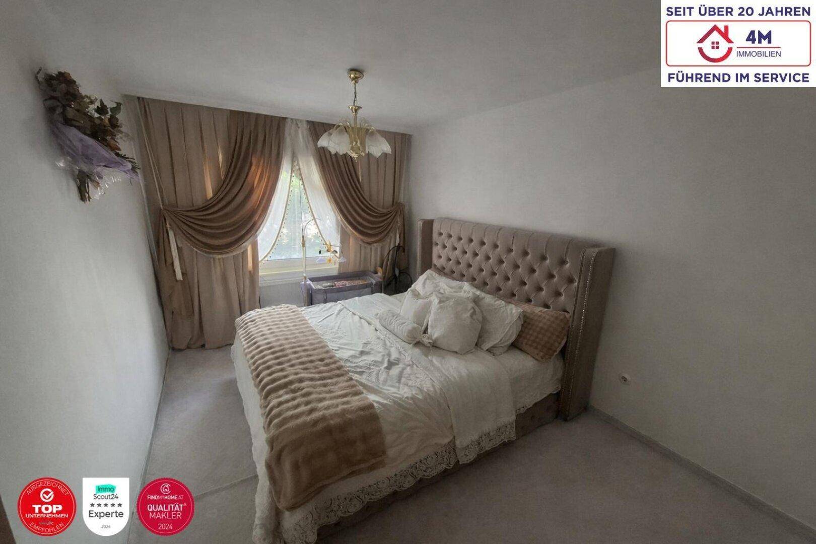 Gemütliches Schlafzimmer mit großem Polsterbett, beigen Vorhängen und weichem Teppichboden.