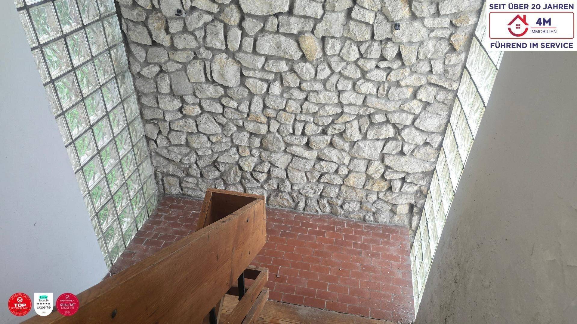 Steinverkleidete Wand und Glasbausteinfenster in einem hellen Treppenhausbereich mit Holzelementen.