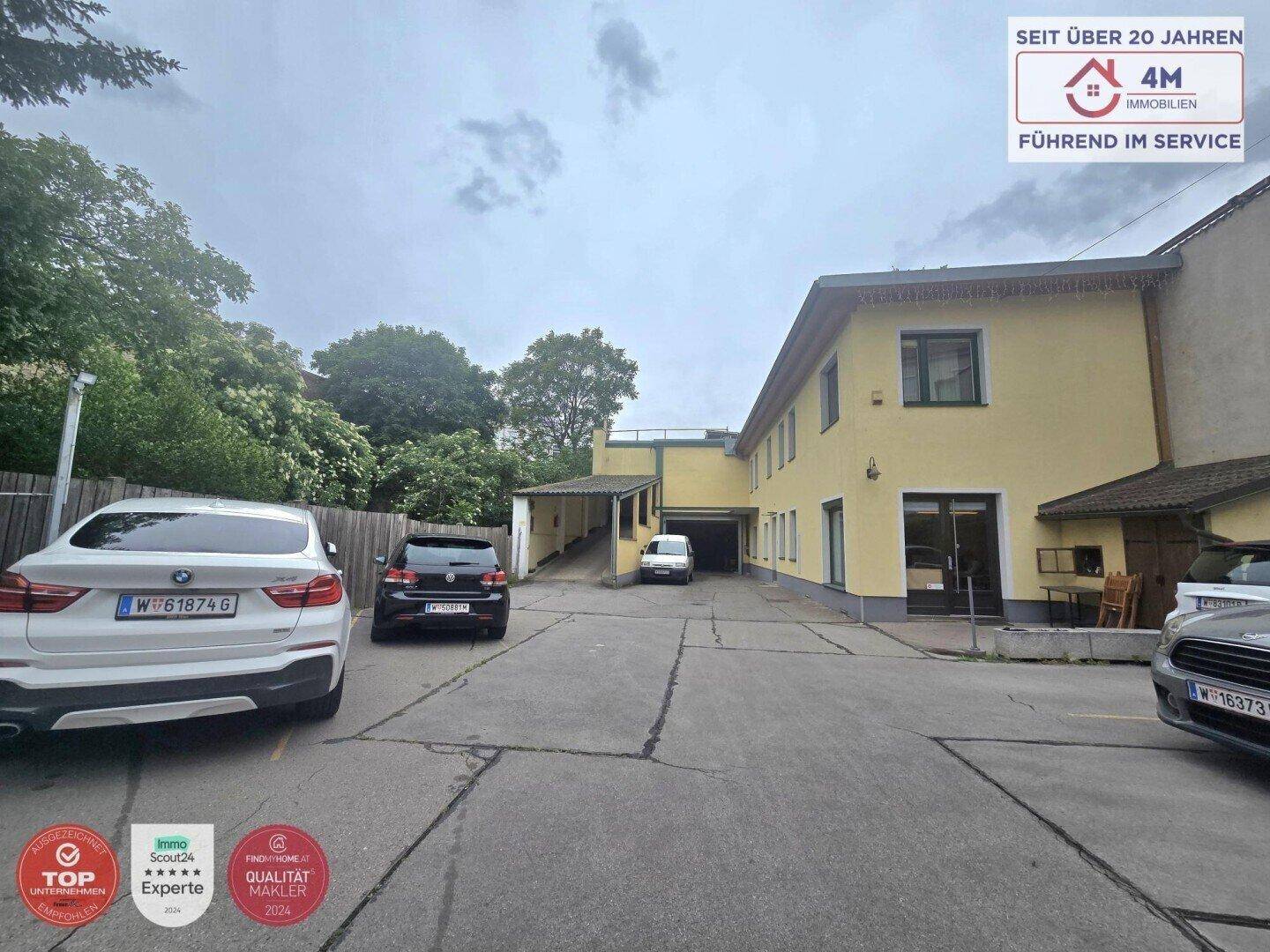 Außenansicht des gelben Gebäudes mit großem Parkplatz und mehreren geparkten Autos unter bewölktem Himmel.