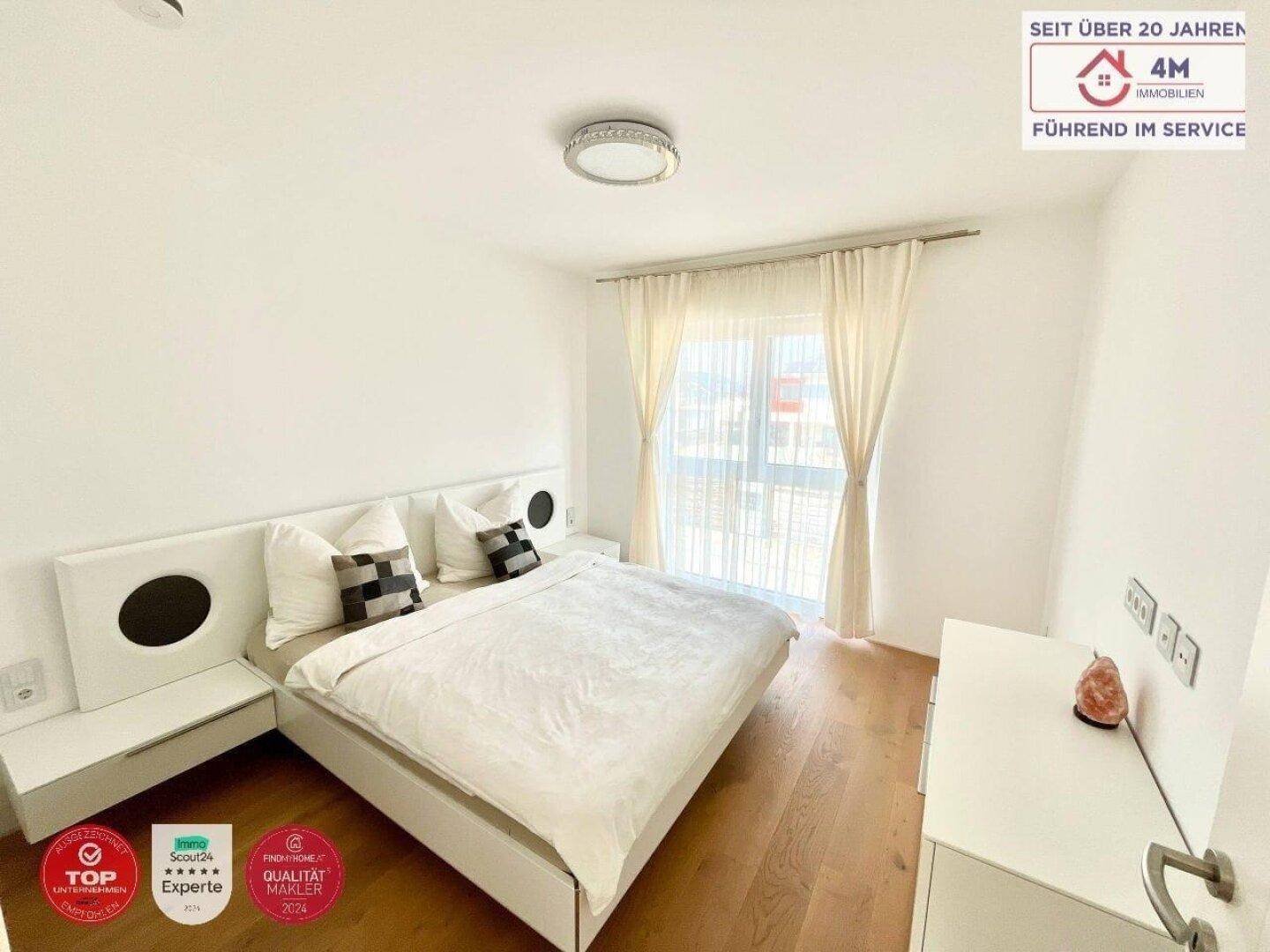 Helles Schlafzimmer mit Doppelbett, Nachttischen und Zugang zu einem Balkon.