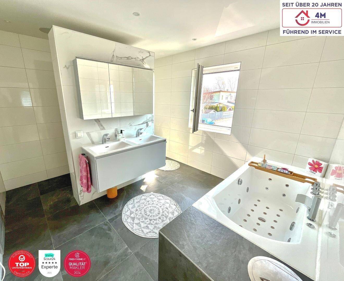 Modernes Badezimmer mit Doppelwaschbecken, Whirlpool-Badewanne und Fenster.