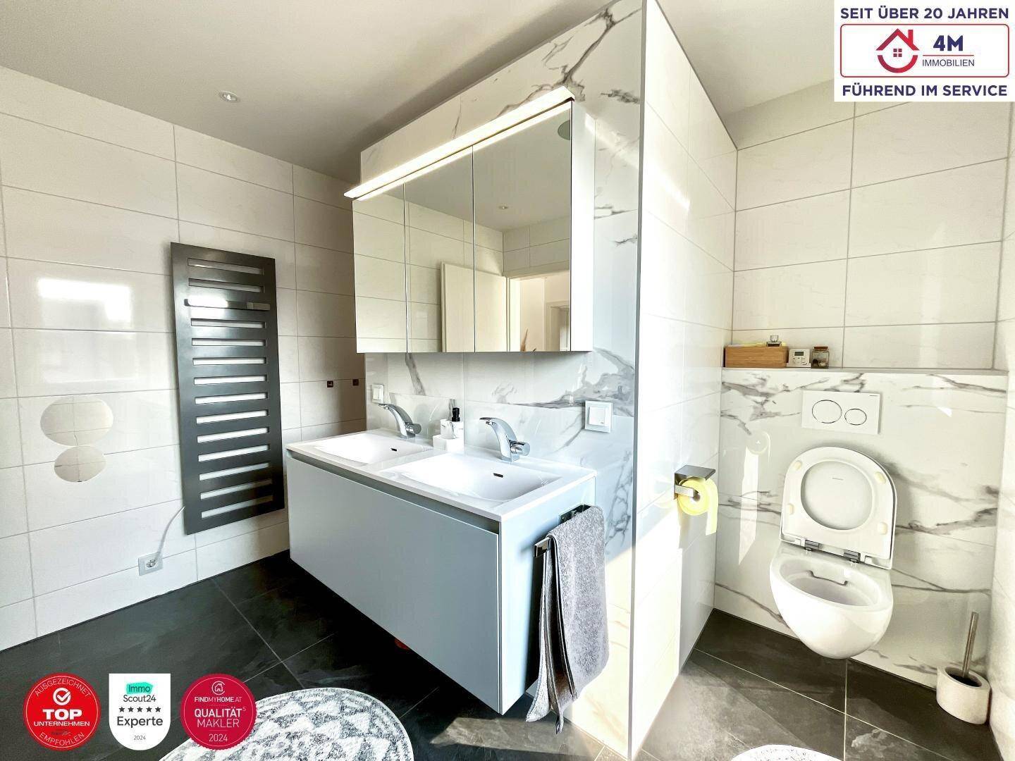 Elegantes Badezimmer mit Doppelwaschbecken, wandhängendem WC und beheiztem Handtuchhalter.