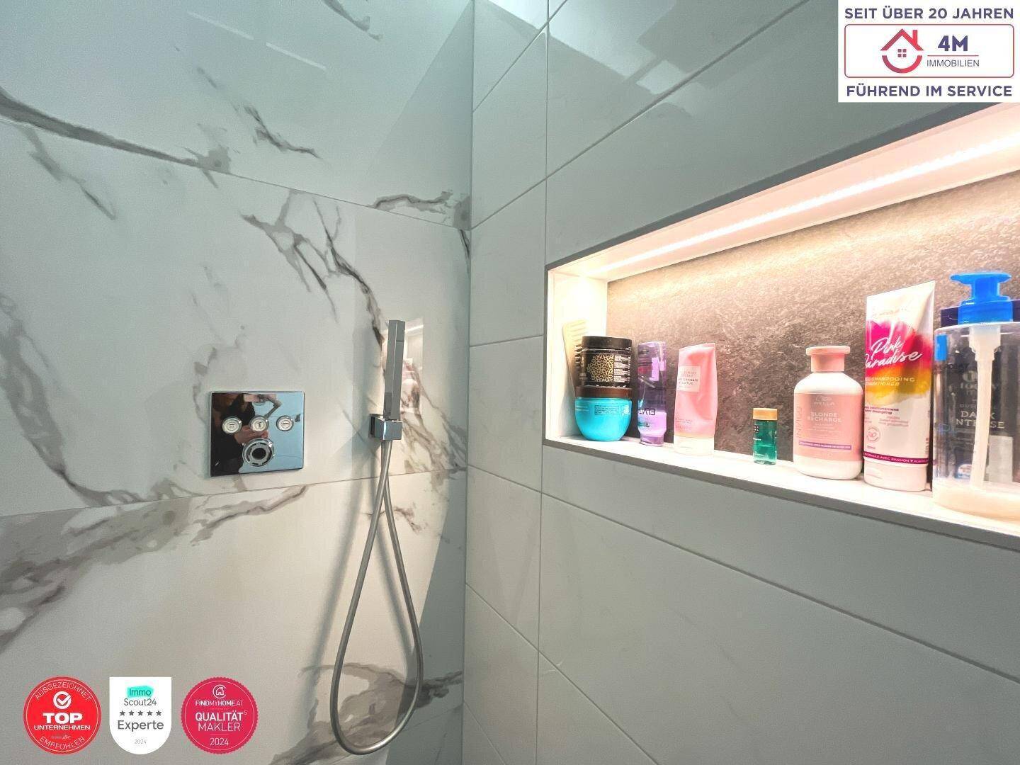 Moderne Dusche mit integrierter Nische für Pflegeprodukte und Marmoroptik-Fliesen.