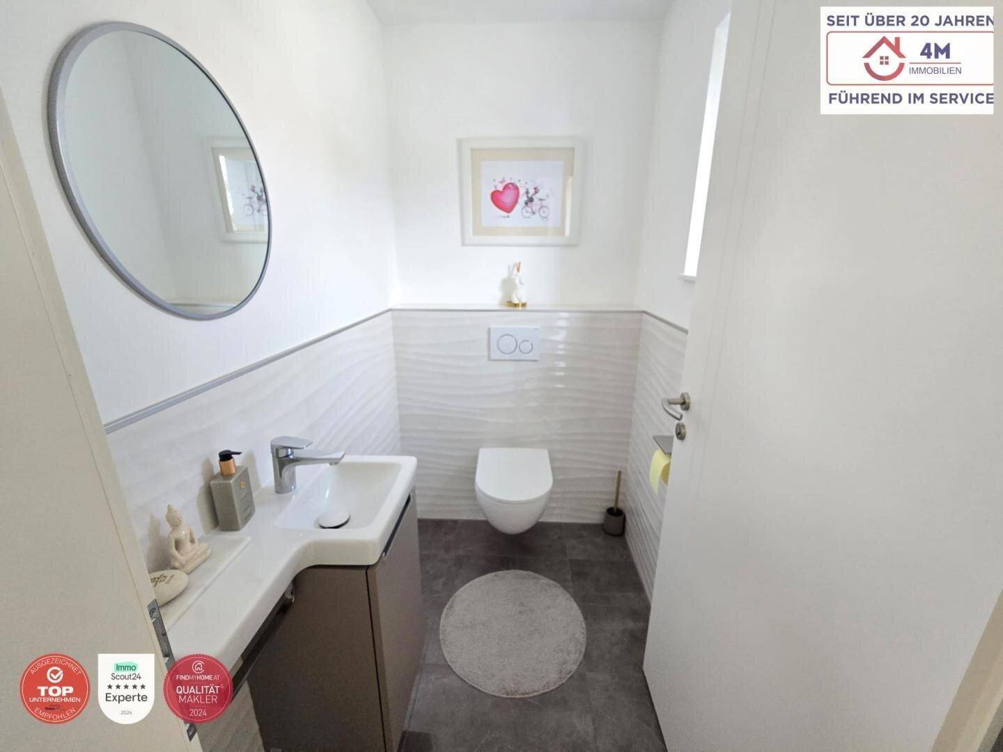 Helles Gäste-WC mit modernem Waschbecken, wandhängendem WC und rundem Spiegel.