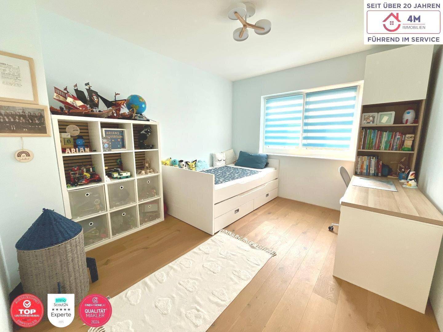 Helles Kinderzimmer mit Einzelbett, Schreibtisch und Spielzeugregal, blauen Wänden.
