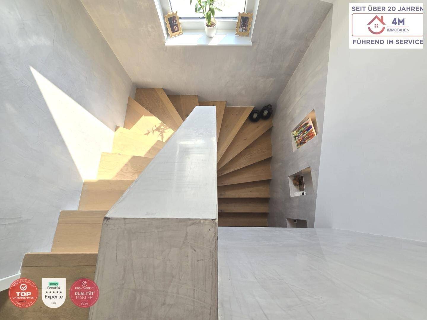 Moderne Holztreppe mit Betonoptik-Geländer und Oberlicht, die die Etagen verbindet.