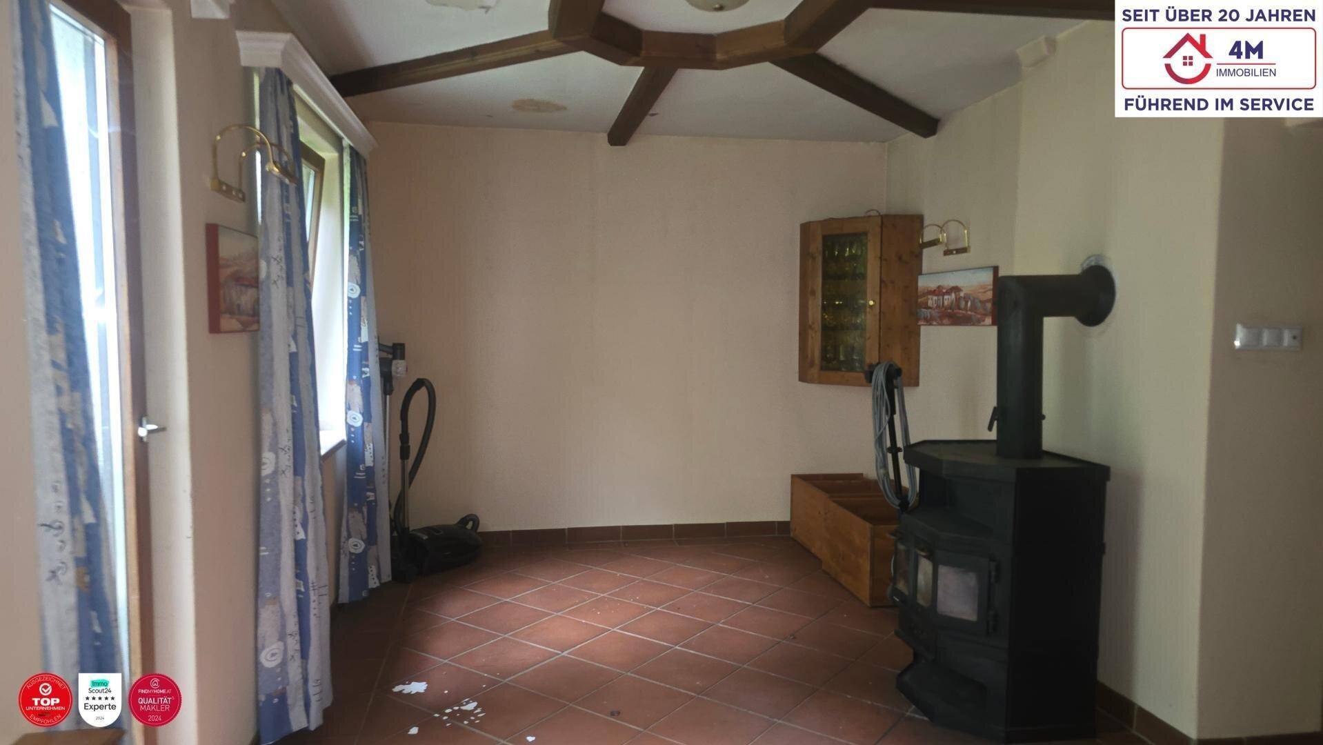 Rustikales Wohnzimmer mit Kaminofen, Terrakottafliesen und sichtbaren Holzbalken an der Decke.