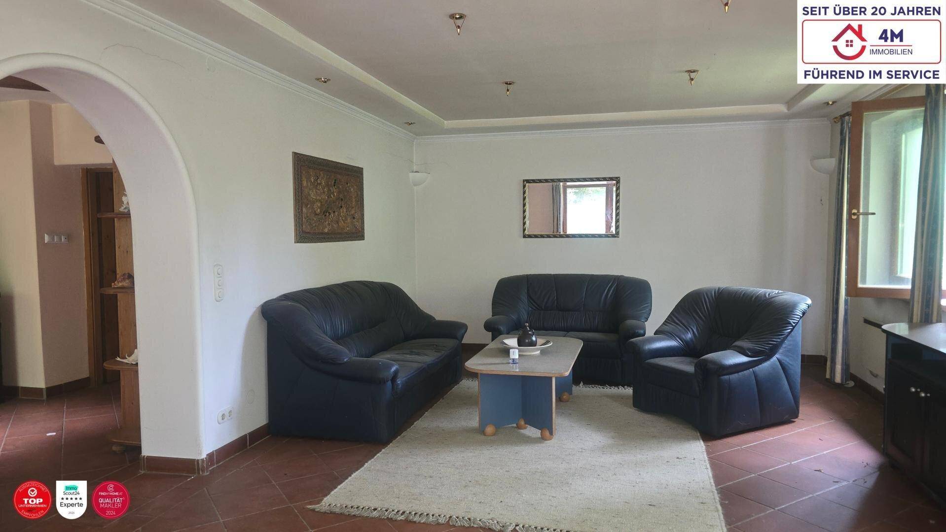 Geräumiges Wohnzimmer mit dunklen Ledersofas, Couchtisch und Terrakottafliesenboden.