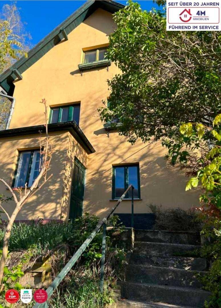 Traditionelles Haus mit gelber Fassade, grünen Fensterrahmen und Steintreppe im Außenbereich.