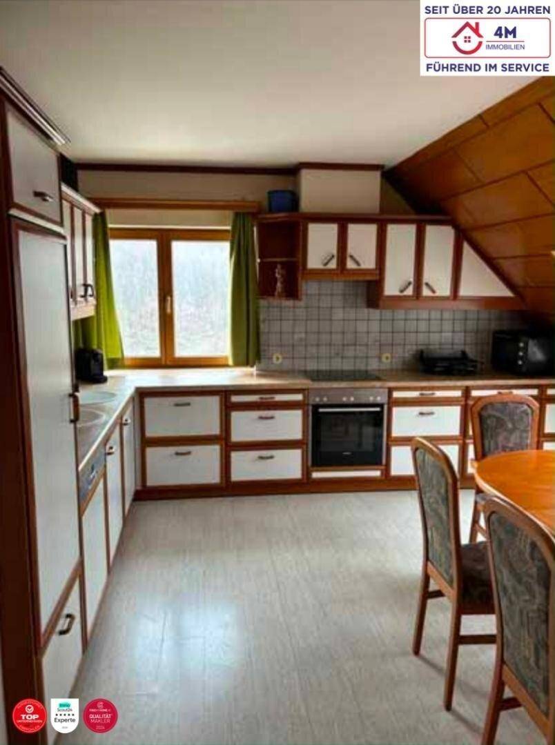 Gemütliche Küche mit Holzelementen, weißen Schrankfronten und Essbereich unter Dachschrägen.
