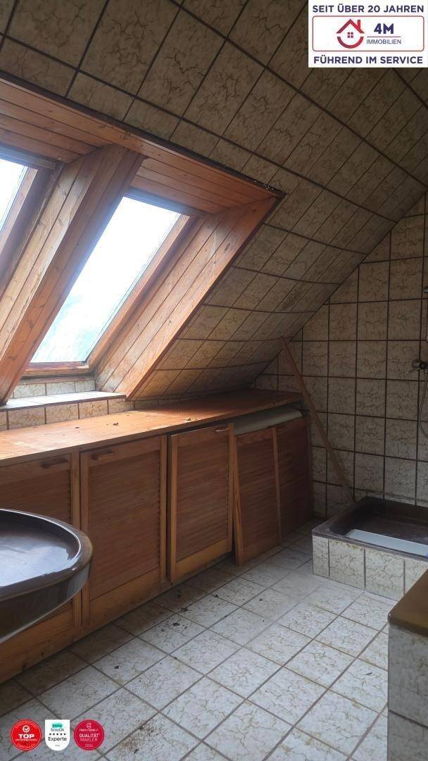 Badezimmer unter Dachschrägen mit Fliesenboden, Holzschränken und Dachfenstern für natürliches Licht.