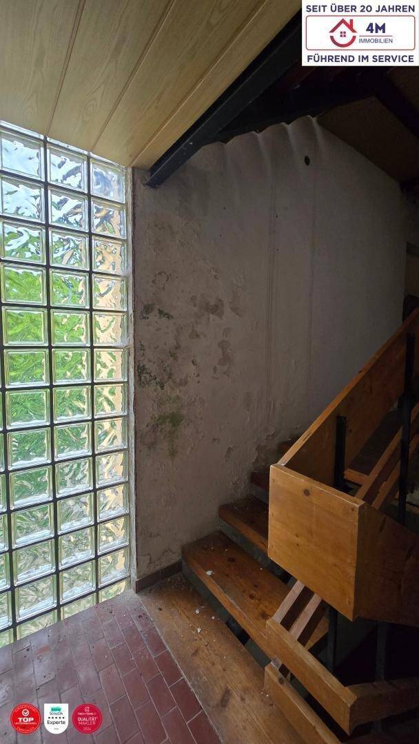 Treppenhaus mit Glasbausteinfenster, Ziegelboden und Holztreppe, die nach oben führt.